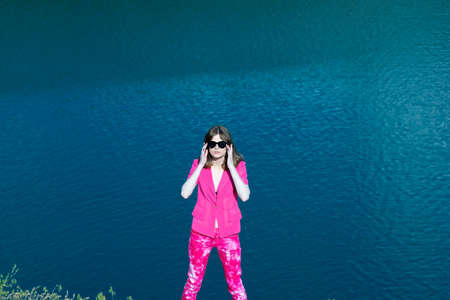 portrait of a fashionable beautiful young girl in pink, generation z. Against the background of the lake water.の写真素材