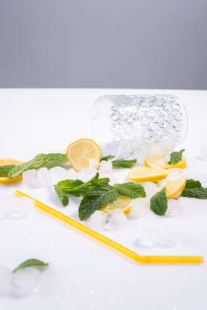 spilled glass of refreshing summer cocktail with ice, lemon and mint on white background.の写真素材