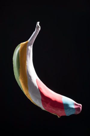 multicolored paint on banana stripes, levitation of multicolored banana on black background.の写真素材