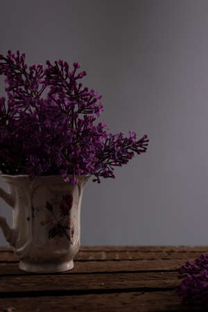 still life of lilac branches in a teacup, on a wooden table, on a gray background. Spring still life in a dark keyの写真素材