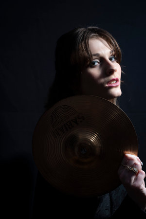 girl model musician in black, holding a snare drum cymbal, looks to the side. On a black backgroundの写真素材