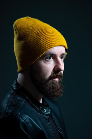 dramatic portrait of a millennial guy in a yellow hat and jacket on a dark background.
