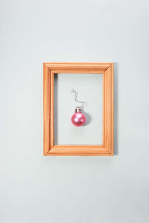 Christmas ball in a wooden photo frame on a pink background. creative minimalism christmas.の写真素材