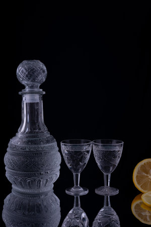 decanter with shot glasses, lemon on black background.