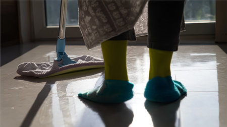 A handsome man in cozy homewear cleans a wooden floor with a mop.の素材