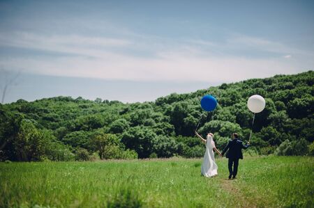 The bride and groom are walking along the lawn with balloonsの写真素材