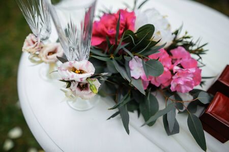 Beautifully decorated wedding glasses for the bride and the groom are on the table. There are flowers and greenery on the tableの写真素材