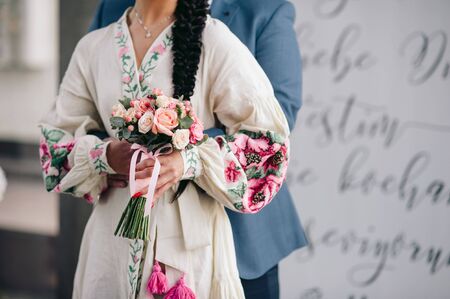 Groom hugs bride in a white dress with embroidery and a long braid, which is holding a bouquetの写真素材
