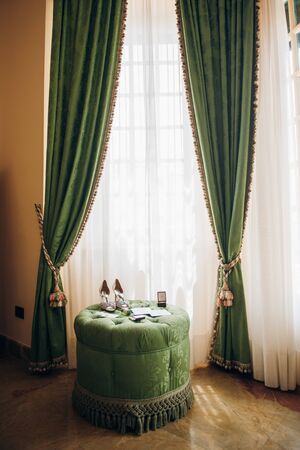 a room in a hotel decorated in green and yellow shades, on a soft puff under the window there are the bride's accessoriesの写真素材
