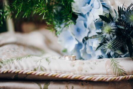 Two wedding rings lie on a pillow, there are fresh blue flowers and greeneryの写真素材