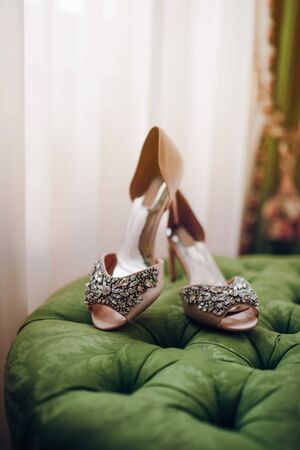 stylish bridal high-heeled shoes decorated with stones stand on a green soft padded stoolの写真素材
