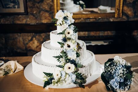 Four tiered white wedding cake decorated with fresh flowers standing on the table