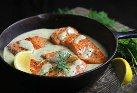 Salmon fillet with creamy sauce in pan.