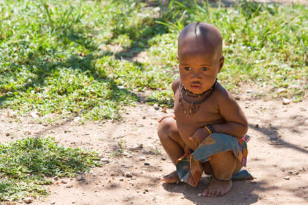 Cute Himba boy sitting in shade and looking away 