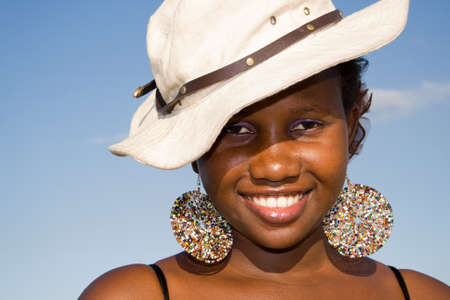 Beautiful african woman laughing and having fun wearing a hat on blue sky background 