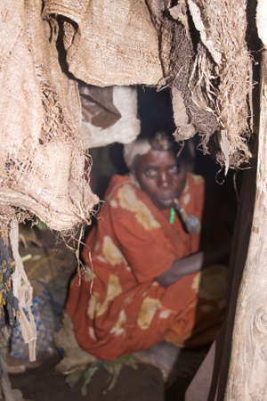 KISORO, UGANDA - DECEMBER 31, 2013  Entrance of a pygmy hut, in the background an unidentified pygmy woman, hidden behind the smoke of her pipe  のeditorial素材