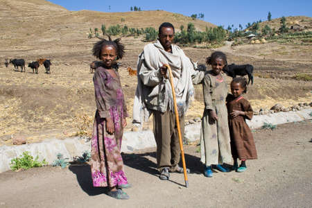 AXUM, ETHIOPIA - FEBRUARY 20, 2010: Unidentified Ethiopian man with his children watch the traffic on the roadside. In the background there is a village.のeditorial素材