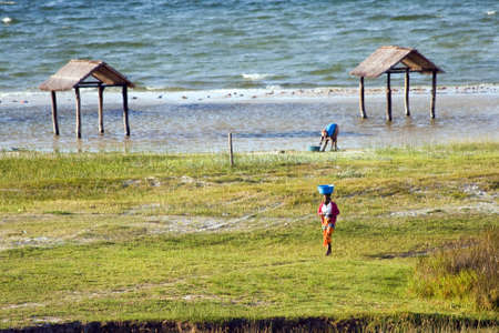 BILENE LAGOON, MOZAMBIQUE ? APRIL 08, 2015: Unidentified woman walks and carries a bucket on the head at the shoreline of the Bilene lagoon.のeditorial素材