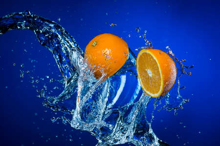 two halves of orange and splash of water on blue background.の写真素材