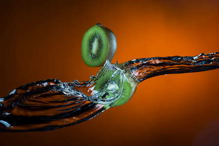 two halves of kiwi and splash of water on orange background.の写真素材