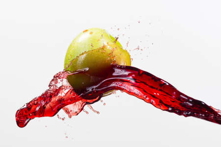 Green apple and splash of red juice in white background.の写真素材