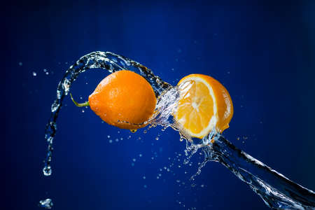 two halves of orange and splash of water on blue background.の写真素材