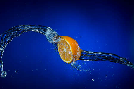 half of orange and splash of water on blue background.