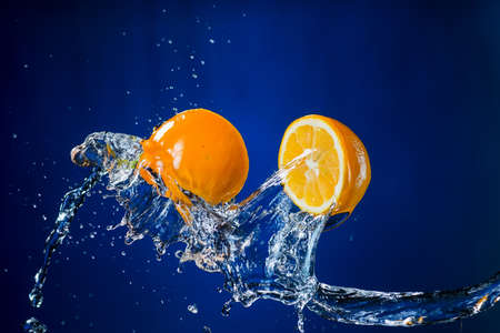 two halves of orange and splash of water on blue background.の写真素材