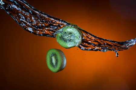 two halves of kiwi and splash of water on orange background.の写真素材