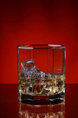 glass of whisky with ice on a red background.の写真素材