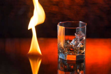 glass of whisky with ice on a red background and fire.の写真素材
