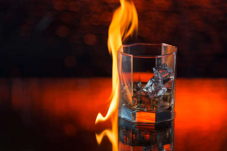 glass of whisky with ice on a red background and fire.の写真素材