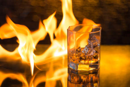 glass of whisky with ice on a black background and fire flames.の写真素材