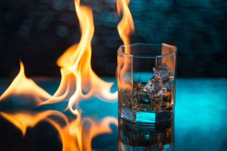 glass of whisky with ice on a blue background and fire flames.の写真素材