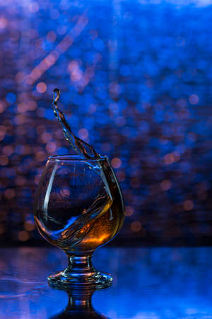 wineglass of cognac and splash on a blue bokeh background.の写真素材