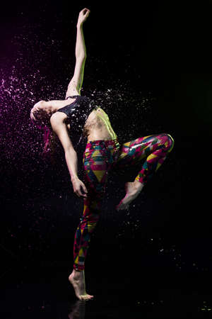 The girl dances on the floor covered with water on a black background and water splashes around her.の写真素材