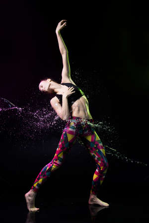 The girl dances on the floor covered with water on a black background and water splashes around her.の写真素材