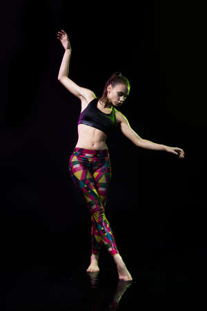 The girl dances on the floor covered with water on a black background and water splashes around her.の写真素材