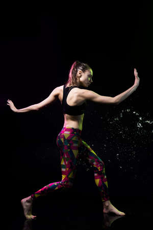 The girl dances on the floor covered with water on a black background and water splashes around her.の写真素材