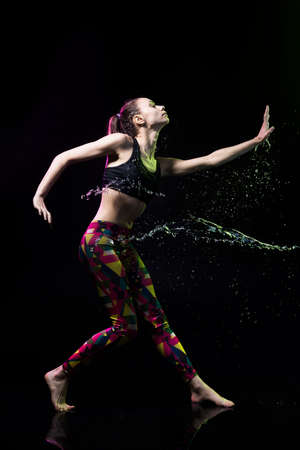 The girl dances on the floor covered with water on a black background and water splashes around her.の写真素材