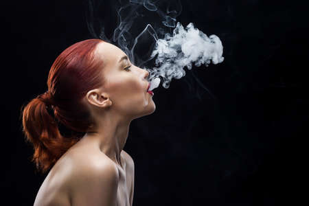 smoking beauty girl portrait on a black background.の写真素材
