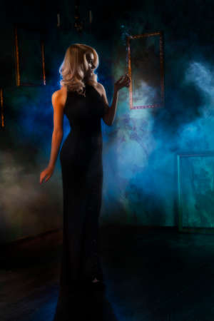 the girl in an evening dress with a cigarette in a hand. blurred retrostyle photo. theatrical fogの写真素材