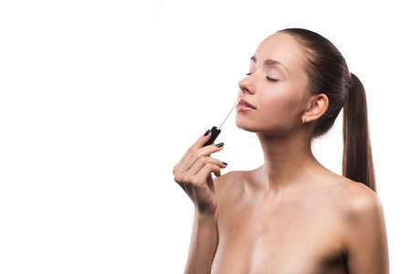 Beautiful young girl with natural make-up puts lip gloss. isolated on white background, copy space. clear healty skin.の写真素材