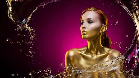 beautiful topless gilded young girl covered with water splash on a violet background. golden bodyart. vanguarg hairstyle. clear healthy skin. an evening make-up. copy spaceの写真素材