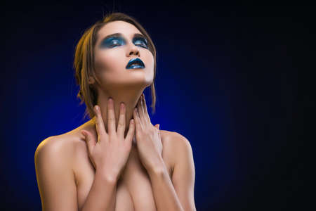 Beautiful mixed asian-caucasian race girl. Advertising and Commercial Design. Shopping. Big Breast. Blue-black background. Blue glossy lips. Healthy clean skin. Evening blue make-up.の写真素材