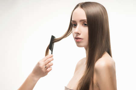 Beautiful young long-haired girl brushed by the stylist. Nude make-up. Naked shoulders. Isolated on...