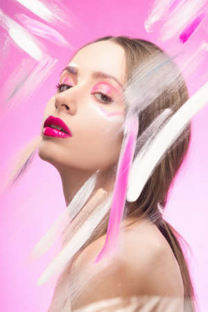The beautiful girl with a vanguard make-up behind the glass covered with paint dabs on a pink background. Copy space. Advertising and Commercial Design. Healthy clean skin.の写真素材