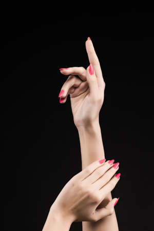 Closeup image of beautiful woman hands with pink manicure on the nails. Cream for palms, manicure and beauty treatment. Elegant and graceful arms with slender graceful fingers. Copy space. Isolated on black.の写真素材