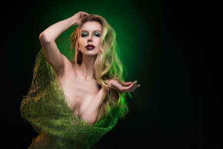Topless girl blonde wrapped in a green network for bouquets, covering her nude breast, with green light on her hair. Dark background. Copy space. Advertising, fashion, concept and commercial Design.の写真素材