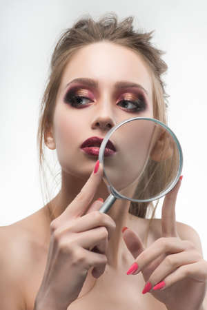 Beautiful naked shoulders girl shows an enlarged with a magnifying glass her healthy skin on her cheeks. Healthy clean skin. Isolated on white background. Cosmetology, spa, skin care. Copy spaceの写真素材